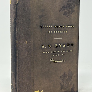 Puede incluir: Un libro de tapa dura marr&oacute;n oscuro, "Little Black Book of Stories" de A.S. Byatt. Letras doradas y dise&ntilde;os florales adornan la portada. La autora es ganadora del Premio Booker.