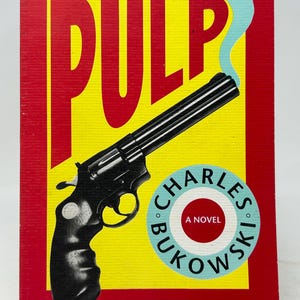 Puede incluir: Portada del libro "Pulp" de Charles Bukowski. La portada presenta un revólver negro con humo saliendo del cañón, sobre un fondo amarillo. El título "PULP" está en letras amarillas grandes, con un borde rojo.
