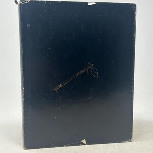 Puede incluir: Un libro negro con una ilustración dorada de un tomahawk. La portada es lisa con algo de desgaste. El diseño del tomahawk está centrado y detallado.