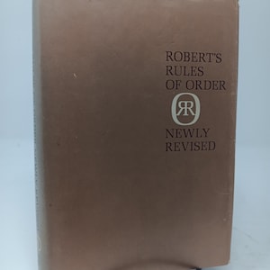 May include: A brown book with the title "Robert's Rules of Order" and a large "R" in a circle. The book is newly revised.