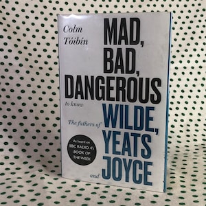 May include: A book titled "MAD, BAD, DANGEROUS to know" by Colm Tóibín. The cover features bold black and blue text with the names Wilde, Yeats, and Joyce. The book is described as "The fathers of" and was heard on BBC Radio 4's Book of the Week.