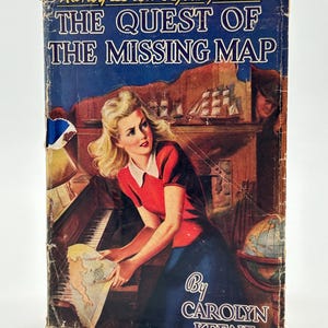 May include: Vintage hardcover book titled "Nancy Drew Mystery Stories: The Quest of the Missing Map" with a blue cover. The cover art features a woman in a red top and blue skirt holding a map. The author is Carolyn Keene.