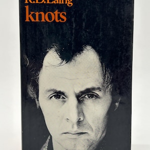 May include: A vintage book cover featuring a black and white portrait of a man. The title "knots" is in orange font, with the author's name, "R.D. Laing," above it. The book cover has a dark background.