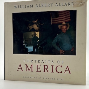 Pode incluir: Um livro de capa dura intitulado "Portraits of America" de William Albert Allard. A capa apresenta uma fotografia de um homem com chapéu de cowboy, uma bandeira americana e um crânio de touro. O título do livro está em letras grandes, cor de vinho.