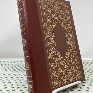 Pode incluir: Um livro encadernado em vinho com letras douradas na lombada que lê "Tales of Fire" de "L'Engle". A capa apresenta um design floral dourado.