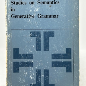 May include: A vintage book titled "Studies on Semantics in Generative Grammar" by Noam Chomsky. The book has a light blue cover with dark blue text and a geometric design. The cover shows signs of wear.