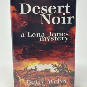 May include: A book titled "Desert Noir" by Betty Webb. The cover shows a desert scene with a fiery sunset and the text "a Lena Jones mystery."