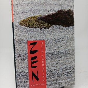 May include: A book titled "Zen Rock Gardening" by Abd al-Havy Moore. The cover features a close-up of a Zen garden with white gravel and a single green moss-covered rock.