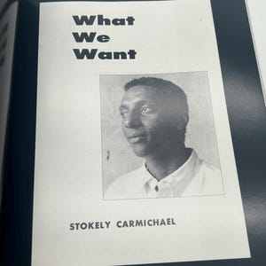 May include: A black and white image of a book page featuring the title "What We Want" in bold, black letters. Below the title is a black and white portrait of Stokely Carmichael.