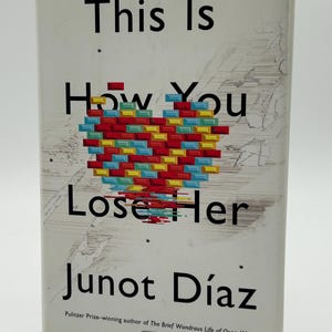 Puede incluir: Un libro titulado "This Is How You Lose Her" de Junot Díaz. La portada presenta un diseño de corazón hecho de bloques rectangulares coloridos. El nombre del autor y una mención del Premio Pulitzer están debajo.