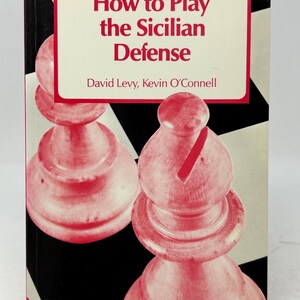 K&ouml;nnte beinhalten: Buchcover "How to Play the Sicilian Defense" aus der The Macmillan Chess Library. Es zeigt ein rot-wei&szlig;es Schachfigurendesign auf einem schwarz-wei&szlig; karierten Hintergrund. Autoren sind David Levy und Kevin O'Connell.