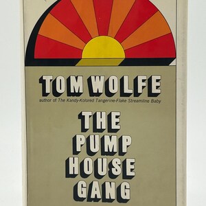 以下が含まれることがあります： トム・ウルフ著「The Pump House Gang」のヴィンテージブックカバー。赤、オレンジ、黄色のサンバーストグラフィックが特徴のレトロなデザインです。タイトルは太字の白い3D文字で、著者の名前は上部にあります。
