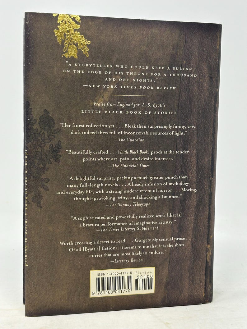 Puede incluir: Contraportada de libro con fondo oscuro y texturizado, adornada con detalles florales dorados. Se ven citas de rese&ntilde;as y el t&iacute;tulo "Little Black Book of Stories", junto con el ISBN.