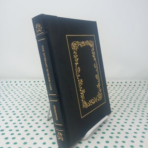 May include: A black leather-bound book with gold lettering on the spine. The title is "The Durrant Murder Case" by Pedroto.