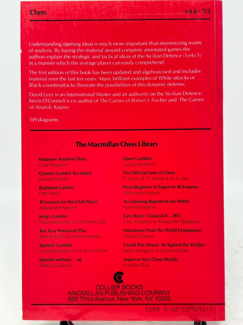 K&ouml;nnte beinhalten: Ein rotes Buch mit dem Titel "Chess" mit einem Preis von 8,95 $. Die R&uuml;ckseite listet verschiedene Schachb&uuml;cher aus der Macmillan Chess Library auf, darunter Titel wie "Kasparov Teaches Chess" und "Open Gambits."