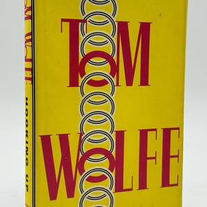 May include: A yellow hardcover book with the title "Tom Wolfe" in large red letters. The cover design includes a chain of interlocking circles. The spine displays the title "Hooking Up".