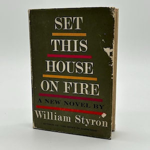 May include: A vintage book titled "Set This House On Fire" by William Styron. The book cover is dark green with the title in large white letters and horizontal orange, pink, and red lines. The author's name is in white.