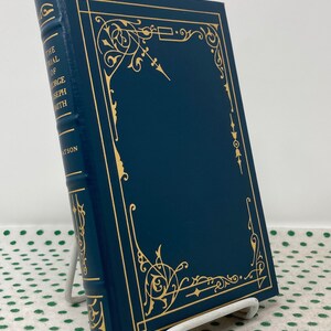 May include: A dark blue hardcover book with gold lettering on the spine. The title is "The Trial of George Joseph Smith". The book is on a white book stand and a green background with white polka dots.