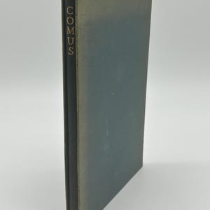 May include: A vintage book titled "Comus" with a dark green cover and spine. The title is printed vertically in gold lettering on the spine. The book's edges show signs of wear, suggesting its age.