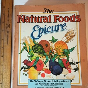 May include: The cover of a cookbook titled "The Natural Foods Epicure: The No Sugar, No Artificial Ingredients, All Natural Foods Cookbook by Nancy Albright, Author of the Rodale Cookbook". The cover features a colorful illustration of a bowl overflowing with fresh vegetables and fruits.