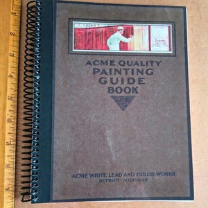 Puede incluir: Un libro encuadernado en espiral titulado "ACME QUALITY PAINTING GUIDE BOOK" con una cubierta marrón. La cubierta presenta una ilustración de un pintor y el texto "ACME WHITE LEAD AND COLOR WORKS DETROIT MICHIGAN". Una regla de madera está en el lado izquierdo.