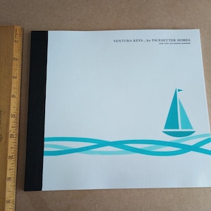 Op de afbeelding: Een witte brochure met een zwarte rand en de tekst "VENTURA KEYS... by PACESETTER HOMES" bovenaan. Een blauwe zeilboot met een wit zeil bevindt zich op een turquoise golfpatroon aan de onderkant van de brochure.