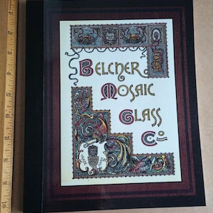 May include: A vintage-style logo for Belcher Mosaic Glass Co. The logo features a decorative border with a stylised bird and floral motifs. The text is in a decorative font with gold accents.