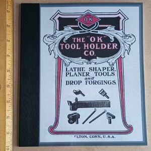 May include: A vintage advertisement for The "OK" Tool Holder Co. featuring a red and black logo with the text "The "OK" Tool Holder Co.". The ad also includes the text "Lathe Shaper, Planer Tools and Drop Forgings." and the company's location, "Fulton, Conn., U.S.A.".
