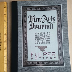 Puede incluir: Una portada de libro vintage para la "Fine Arts Journal" dedicada a las bellas artes y las artes decorativas, la mejora cívica y el embellecimiento del hogar. La portada presenta un borde decorativo y el texto "Fulper Pottery".