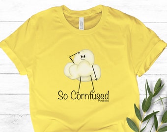 May include: A yellow t-shirt featuring a cartoon popcorn character with a confused expression. The text "So Cornfused" is printed below the character. The shirt is made of a soft material and has rolled-up sleeves.