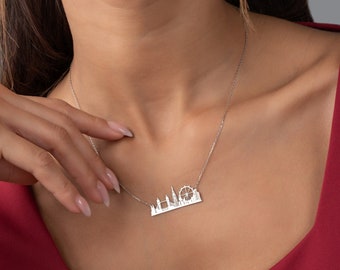Puede incluir: Un collar de plata con un colgante de la silueta de Londres. El colgante presenta el London Eye, el Big Ben y otros monumentos emblemáticos.