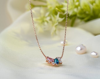 May include: A delicate gold necklace with a pendant featuring a cluster of small sparkling stones, including a pink and a blue gemstone.