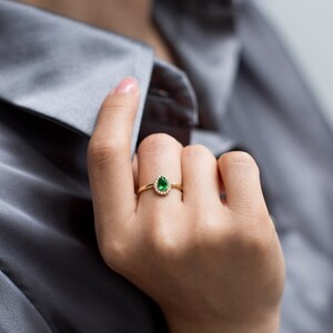 May include: A gold ring with a pear-shaped green gemstone surrounded by a halo of smaller diamonds.
