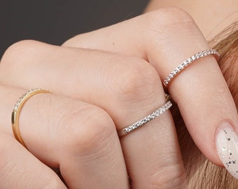 May include: A hand wearing three thin diamond rings. The rings are all set in metal and have a simple, elegant design. The hand is also wearing a light pink nail polish with glitter.