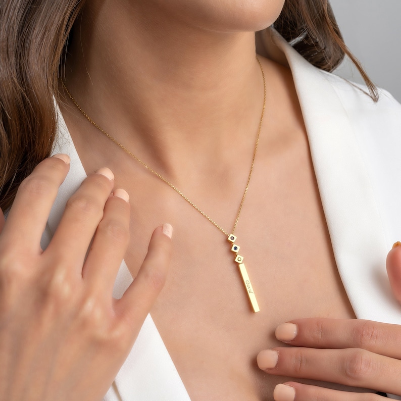 May include: A gold necklace with a vertical bar pendant that says "Jared" and three small square charms with black stones.