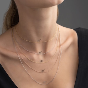 May include: A model is wearing five different chain necklaces in gold and silver. The necklaces are labelled with their lengths: 14 inches, 16 inches, 18 inches, 20 inches, and 22 inches.
