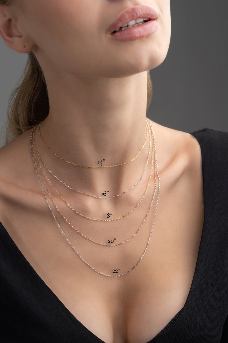 May include: A model is wearing five different chain necklaces in gold and silver. The necklaces are labelled with their lengths: 14 inches, 16 inches, 18 inches, 20 inches, and 22 inches.