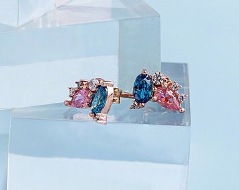 May include: A pair of rose gold earrings with blue and pink gemstones. The earrings feature a cluster of small stones surrounding a larger oval-shaped stone.