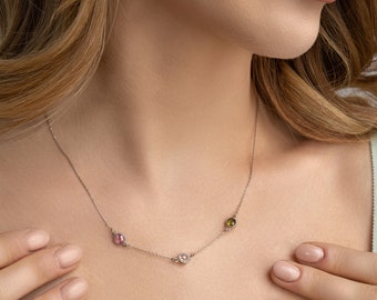 May include: A silver chain necklace with three small round gemstones. The gemstones are pink, clear, and green.