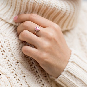 May include: A rose gold ring with a pear-shaped pink gemstone surrounded by smaller clear gemstones.