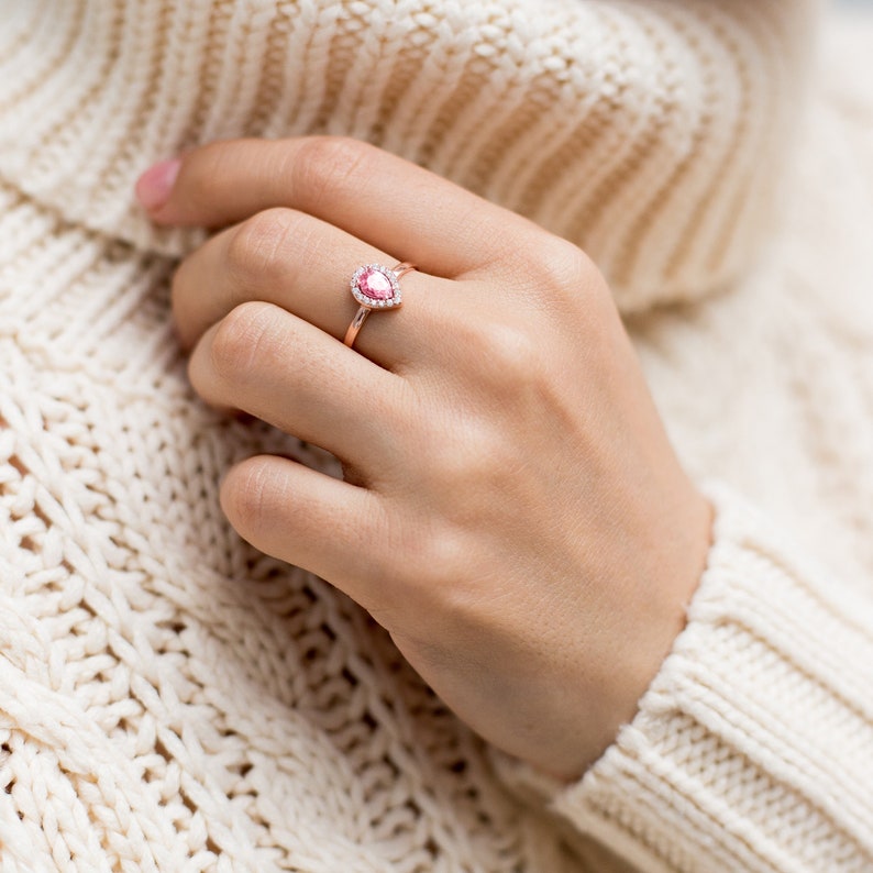 May include: A rose gold ring with a pear-shaped pink gemstone surrounded by smaller clear gemstones.