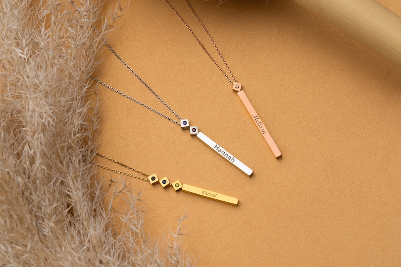 May include: Three gold necklaces with personalised name bars. The necklaces feature small cubic zirconia stones. The names on the bars are "David", "Hannah", and "Melissa".