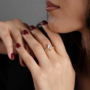 May include: A gold ring with a pear-shaped diamond and smaller diamonds set in the band. The ring is on a person's finger with red nail polish.
