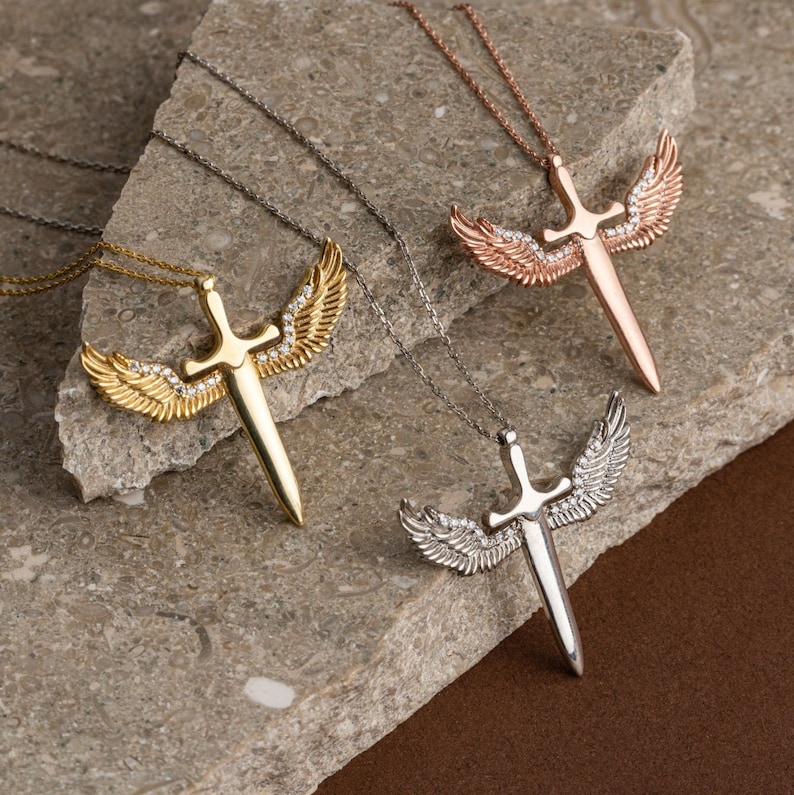 May include: Three silver necklaces with a sword pendant and angel wings. The swords are adorned with clear crystals.