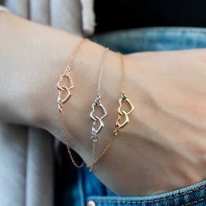 May include: Three gold bracelets with interlocking heart charms. Each heart charm has a small gemstone in the center. The gemstones are blue, purple, and clear.