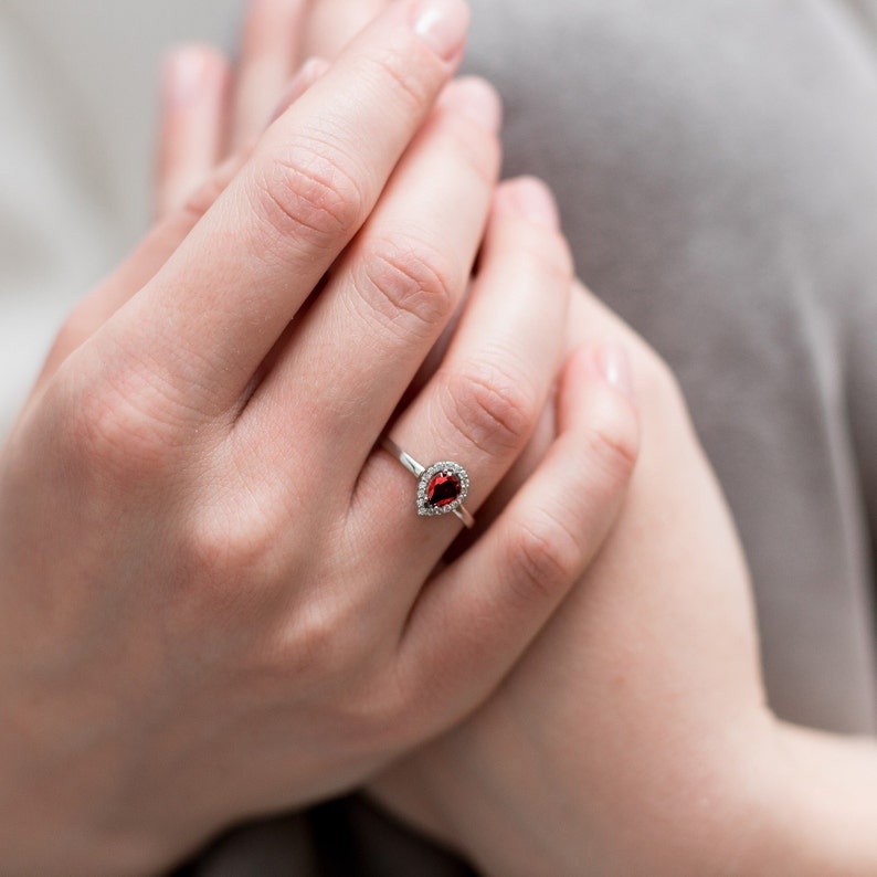 May include: A silver ring with a pear-shaped red gemstone surrounded by smaller white gemstones.