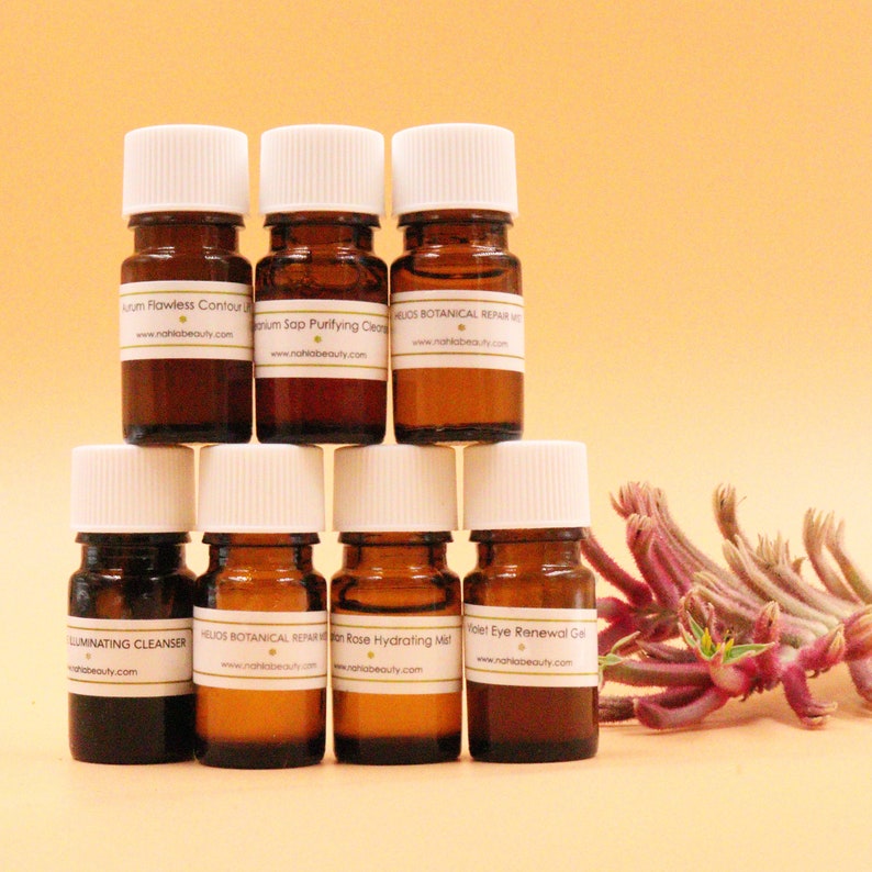 May include: Seven small brown glass bottles with white lids and labels. The bottles are arranged in a pyramid shape. The labels have text that includes the words "Flawless Contour", "Purifying Cleanser", "Botanical Repair", "Illuminating Cleanser", "Hydrating Mist", and "Eye Renewal Gel".