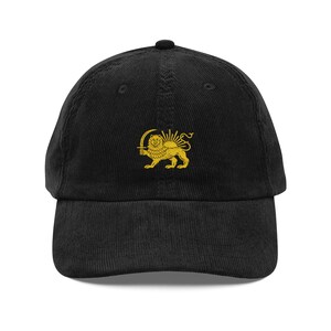 May include: Black corduroy baseball cap with a gold embroidered emblem of a lion holding a sword and sunburst. The cap has a curved peak and an adjustable strap. A fashionable accessory for everyday wear, suitable for various casual outfits.