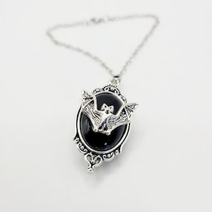 May include: A silver pendant necklace with a black oval cameo featuring a silver bat. The cameo has an ornate silver frame.