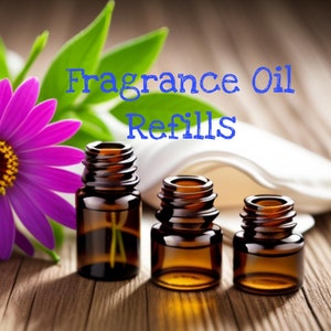 以下が含まれることがあります： 木製の表面に、薄い茶色の液体が入った茶色のガラス瓶が3本置かれています。瓶はそれぞれサイズが異なり、白い背景に青い文字で「Fragrance Oil Refills」と書いてあります。